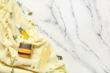 Sarı kumaş, papatya çiçeği, şişe ve mermer zemin üzerinde kozmetik ürünler.