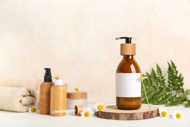 Papatya çiçekleri, yuvarlak ahşap dilimler, şişeler ve bej duvarın yanındaki masada kozmetik ürünler.