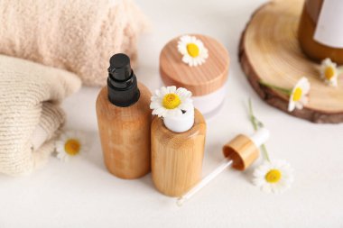 Beyaz arka planda papatya çiçekleri, havlular, şişeler ve kozmetik ürünler kavanozu, yakın plan