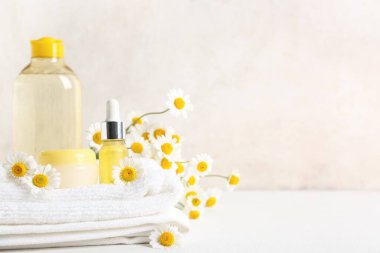 Papatya çiçekleri, havlular, şişeler ve kozmetik ürünleri bej arka plan yakınlarındaki masada, yakın plan
