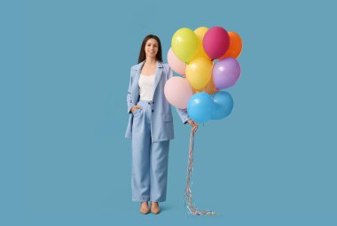 Mavi arka planda renkli balonları olan mutlu genç bir kadın.