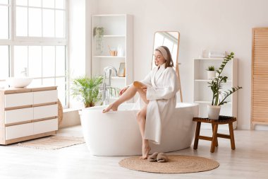 Bacağına banyoda fırçayla masaj yapan genç bir kadın.