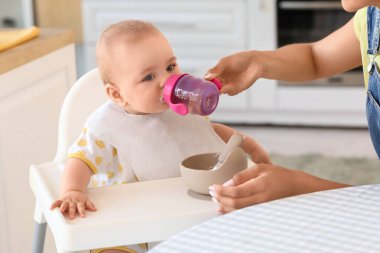 Annem bebeğine evde yüksek sandalyede su veriyor.