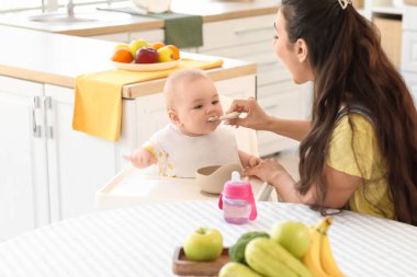 Anne bebeğini evdeki yüksek sandalyede besliyor.