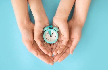 Renk arkaplanında alarmlı saate sahip ailenin elleri