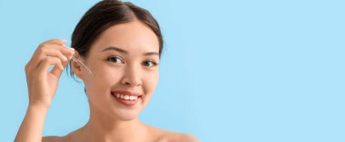 Güzel Asyalı kadın açık mavi arkaplana yüz serumu uyguluyor.