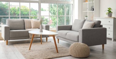 Işıl ışıl oturma odasının içi rahat gri koltuklar, kahve masası ve büyük pencereli.