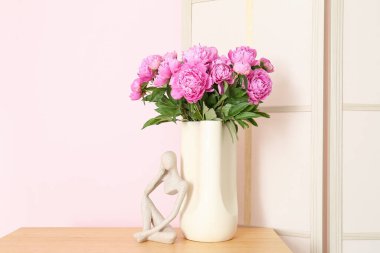 Rafların üzerinde pembe şakayık ve biblo vazosu ve renk duvarına yakın giyinme ekranı var.