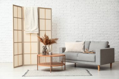 Sıcak gri kanepe, sehpa ve beyaz tuğla duvarın yanında katlanan ekran.