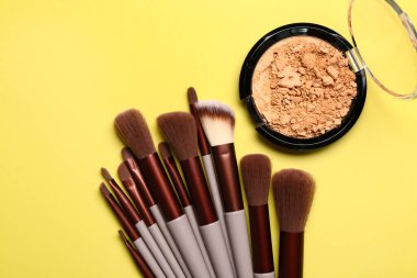 Sarı arka planda makyaj fırçaları ve yüz pudrası.