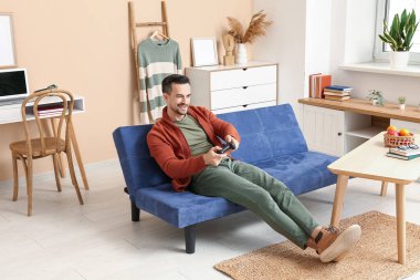 Oturma odasındaki kanepede video oyunu oynayan yakışıklı adam.