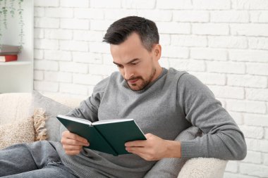 Oturma odasındaki kanepede kitap okuyan yakışıklı adam.