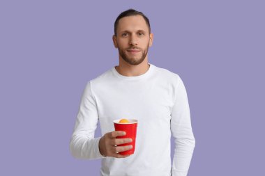 Mor arka planda plastik bardak soğuk birası olan genç adam.