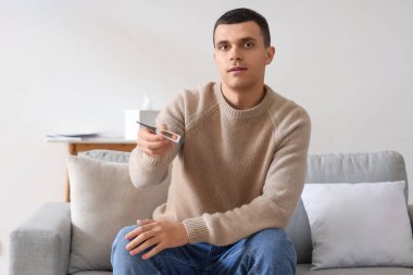 Evde termometre görüntülü konuşan hasta genç adam.