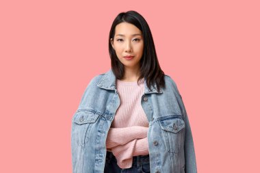 Pembe arka planda şık kot ceketli güzel bir Asyalı kadın.