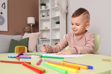 Masada keçeli kalemlerle çizen komik küçük çocuk.