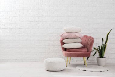 Yastıklı koltuk, ev bitkisi ve beyaz tuğla duvarın yanında puf.