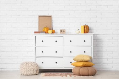 Yastıklı puf ve beyaz tuğla duvarın yanındaki çekmeceler.