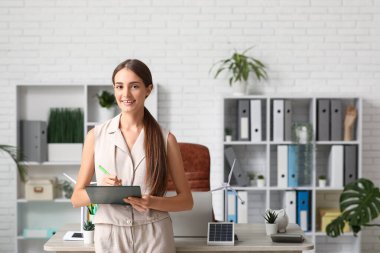 Ofisteki masasında pano ve rüzgar türbini modeli olan genç bayan mühendis.