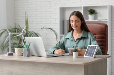 Ofiste çalışan hesap makinesi ve rüzgar türbini modelli kadın mühendis.