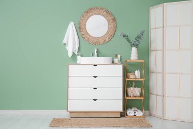 Modern lavabo, çekmeceler ve banyoda yeşil duvarın yanında katlanan ekran.