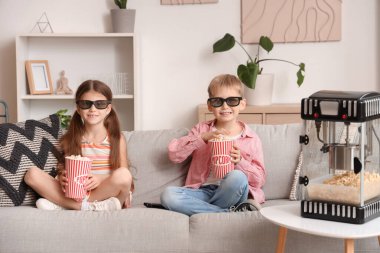 Üç boyutlu gözlüklü, patlamış mısırlı küçük çocuklar evdeki kanepede film izliyorlar.