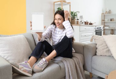 Evdeki kanepede boş tablet bilgisayarlı güzel bir kadın oturuyor.