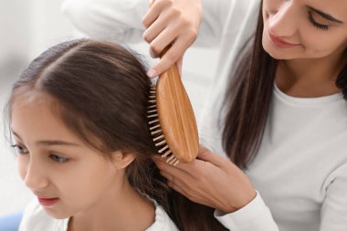 Genç anne banyoda küçük kızının saçını tarıyor, yakın plan.