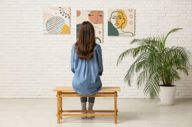 Genç bir kadın sanat galerisinde tablolara bakıyor.