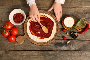 Dişi eller hamura domates ezmesi sürüyorlar pizza için ahşap arka planda
