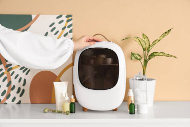 Kadın eli ve kapalı küçük kozmetik buzdolabı. Cilt ürünleri, bej duvarın yanındaki çekmecelerde. Yakın çekim.