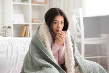 Yatak odasında sıcak ekose kumaşlı donmuş genç bir kadın oturuyor.