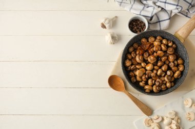 Kızarmış mantarlı tava, sarımsak ve beyaz ahşap arka planda bir kase biber.