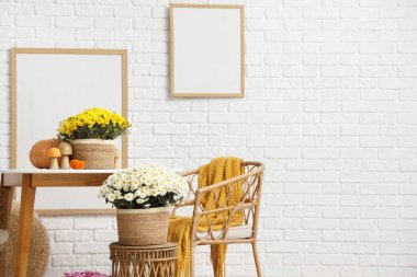 Yemek masası ve kasımpatı çiçekleri beyaz tuğla duvarın yanında.