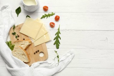 Lezzetli işlenmiş peynir dilimleri, taze sebzeler ve beyaz ahşap masada ekmek.