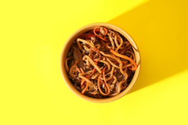 Bir kase lezzetli Çin eriştesi, sebzeli ve sarı arka planda et.