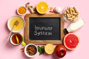 IMMUNE SİSTEM yazılı tebeşir tahtası, farklı sağlıklı yiyecekler ve pembe arka planda haplar