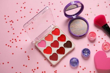 Parıltı kavanozları, konfeti, makyaj ürünleri ve pembe arka planda fırçayla kompozisyon