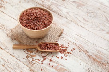 Bej ahşap arka planda çiğ kahverengi pirinçli kase ve kepçe.