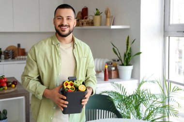 Mutfakta yemek pişirirken gübre kutusu ve sebze artıklarıyla gezen genç adam.