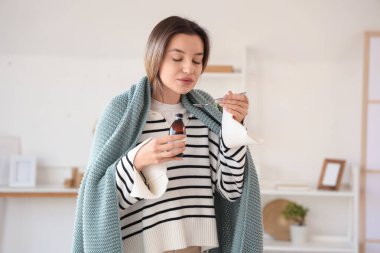 Ekoseli hasta genç kadın evde öksürük şurubu içiyor.