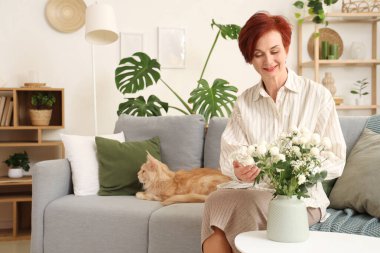 Çiçek vazosu ve sevimli Maine Rakunu kedisi olan olgun kızıl kadın.