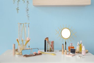 Odadaki mavi duvarın yanındaki masada aynalı makyaj malzemeleri var.