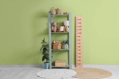 Odadaki yeşil duvarın yanında oyuncakları ve stadyumu olan raf ünitesi.