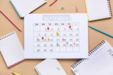 Not defterli takvim, bej arka planda kalemler ve iğneler. Planlama kavramı