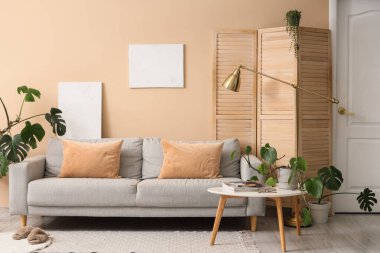 Masa, kanepe ve evin çiçekleri odanın içindeki bej duvarın yanında.