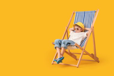 Sarı arka planda güverte koltuğunda oturan sevimli küçük çocuk. Seyahat kavramı