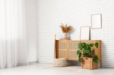 Çekmeceli modern odanın içi ve beyaz tuğla duvarın yanındaki Monstera bitkisi.