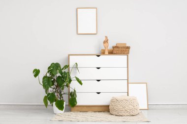 Çekmeceli, pouf ve Monstera bitkisi dolu modern bir oda.