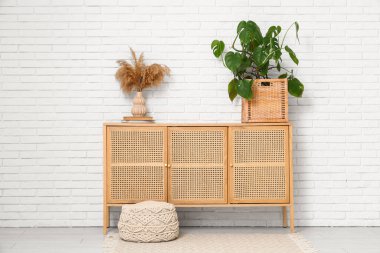 Beyaz tuğla duvarın yanında çekmeceleri ve Monstera bitkisi olan bir oda.